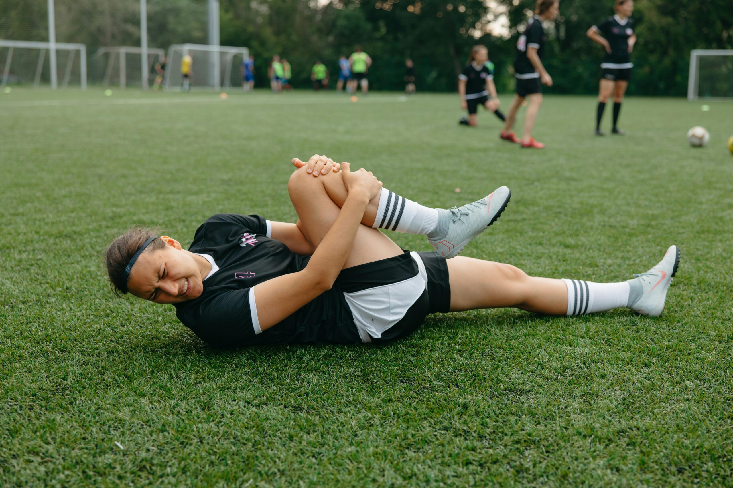 A female soccer player lying on the field, holding her injured leg in pain during a game.